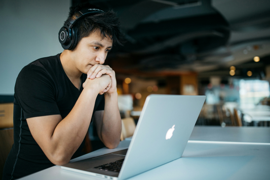 dark haired man in a black shirt sitting at a table looking at an apple computer 