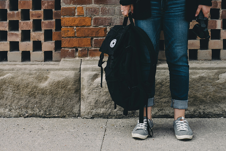 Bottom half of a woman holding a back pack wearing jeans and sneakers