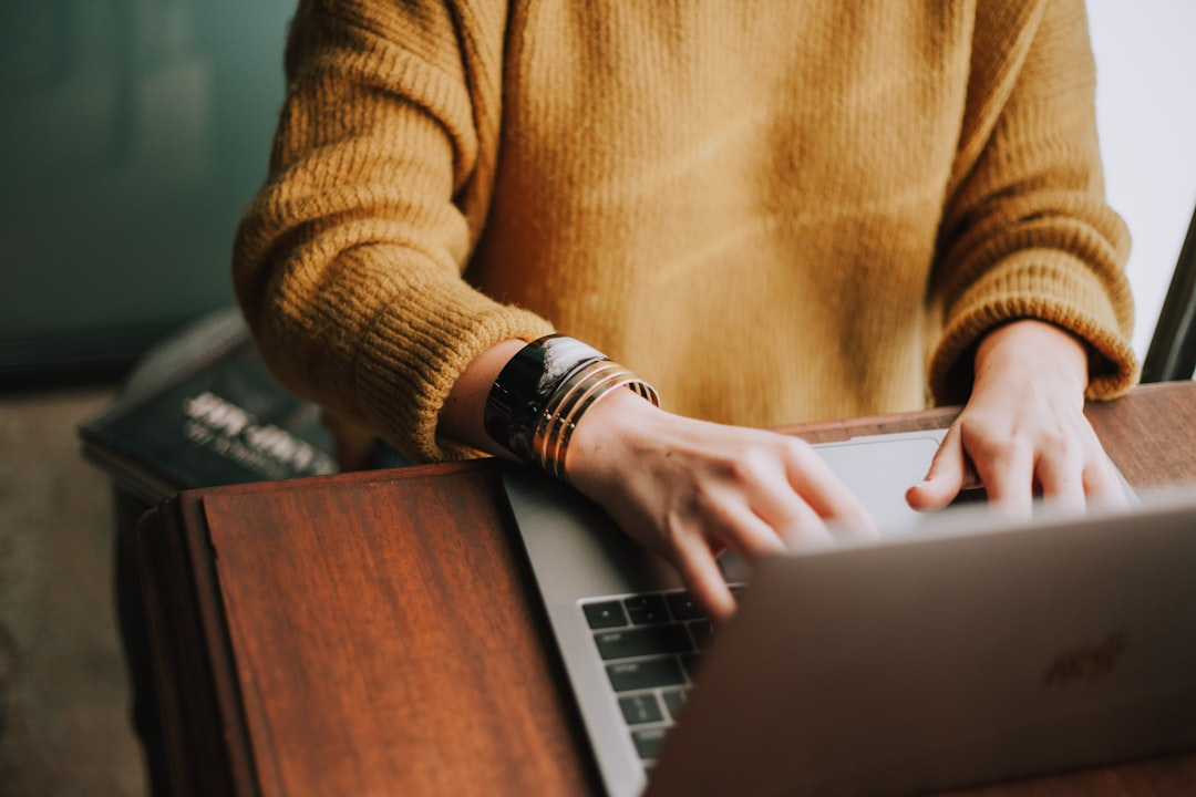 Woman wearing a gold colored sweeter with hands on a lap top computer