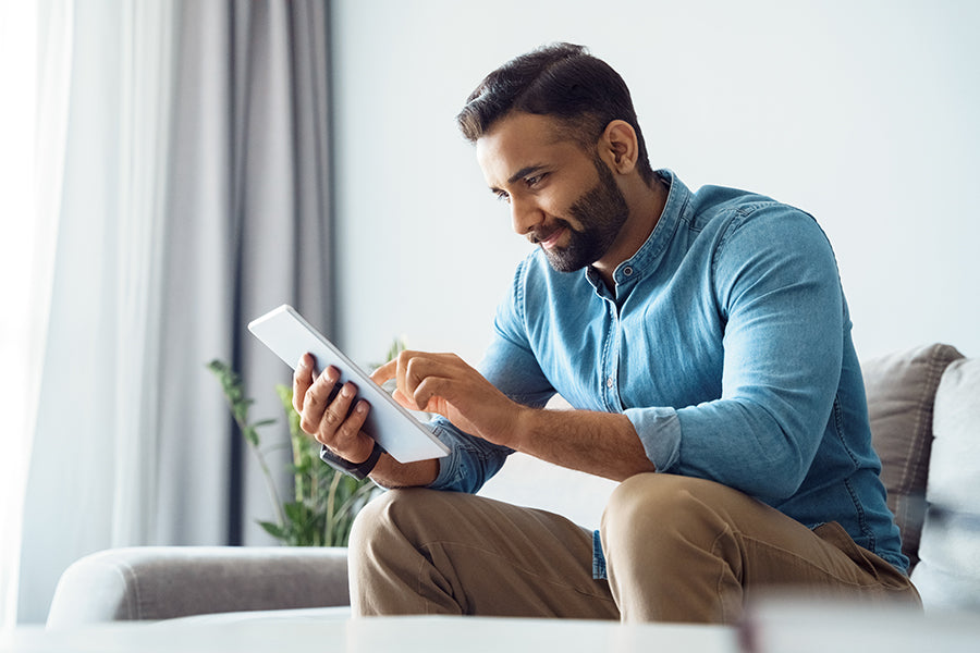 Man sitting on a couch using a tablet in a bright living room.